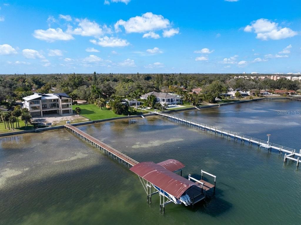 An aerial view shows a long wooden pier with a boat lift extending into water — 6100 BAHAMA SHORES DRIVE S, ST PETERSBURG, FL