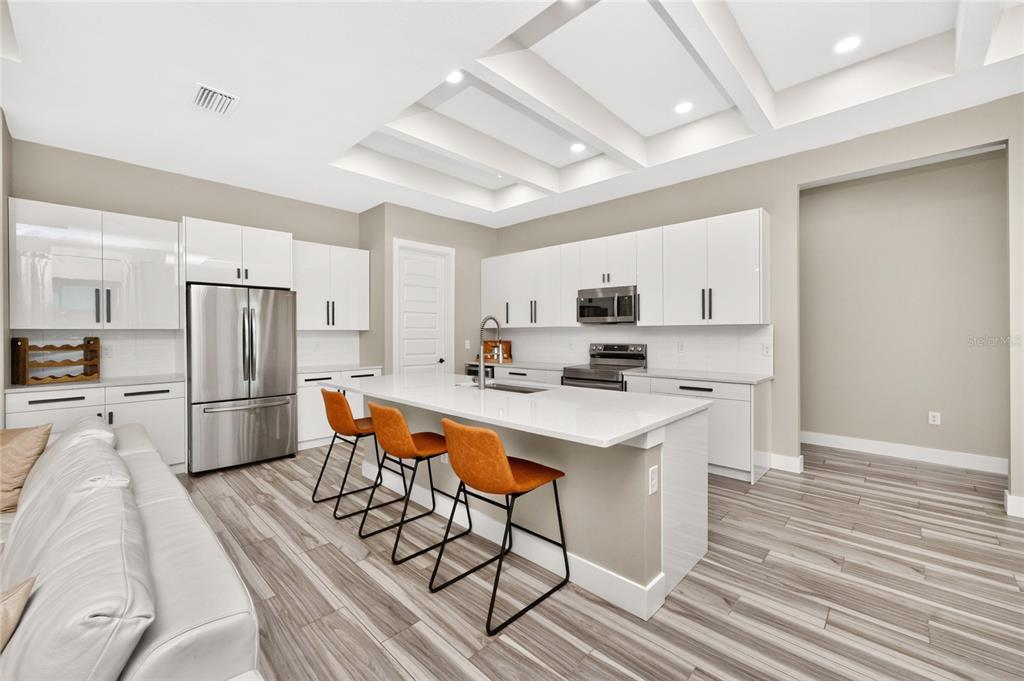 A modern kitchen features white cabinets, a central island with bar stools, and wood-look flooring — 253 LONG MEADOW LANE, ROTONDA WEST, FL