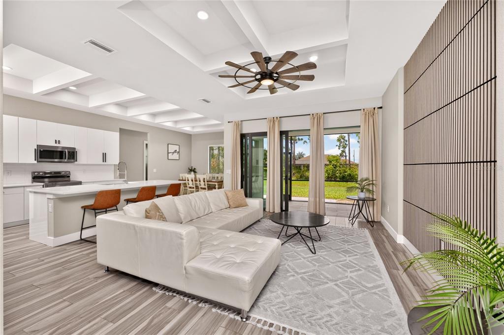 An open-concept living room and kitchen featuring a white sectional, coffered ceilings, and sliding doors — 253 LONG MEADOW LANE, ROTONDA WEST, FL