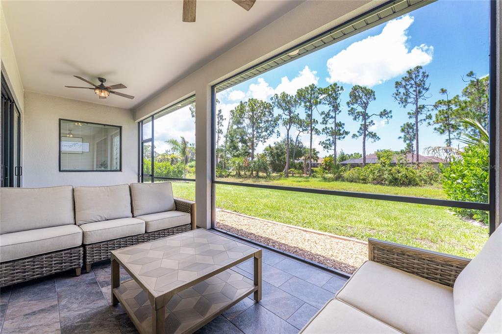A screened-in patio features tiled flooring, wicker furniture, and a view of a grassy yard — 253 LONG MEADOW LANE, ROTONDA WEST, FL