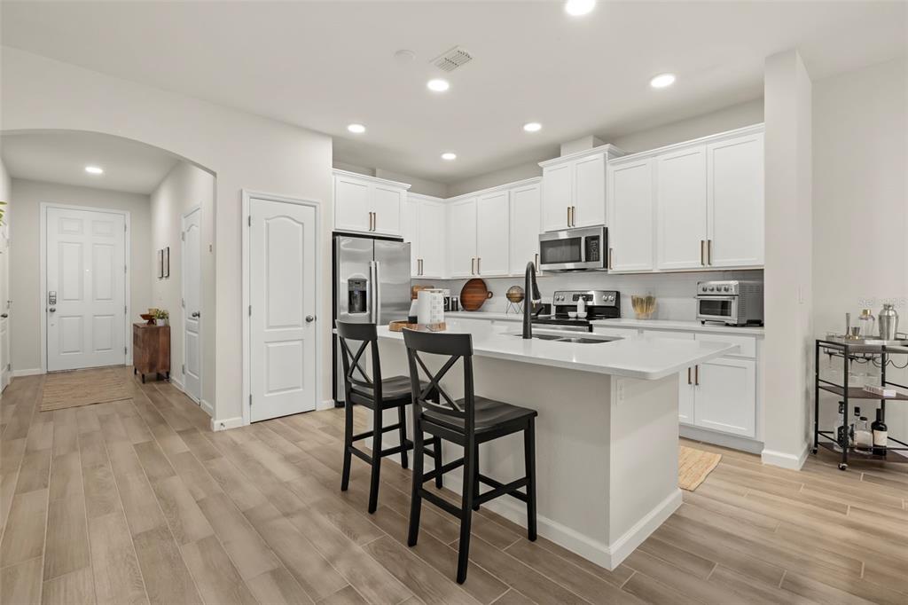 A modern kitchen features white cabinetry, a central island with bar stools, and light wood flooring — 3040 PILOT HOUSE PLACE, OVIEDO, FL