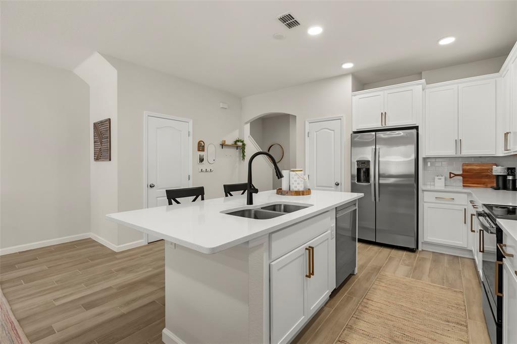 A kitchen features a white island with a sink, stainless steel appliances, and wood-look flooring — 3040 PILOT HOUSE PLACE, OVIEDO, FL