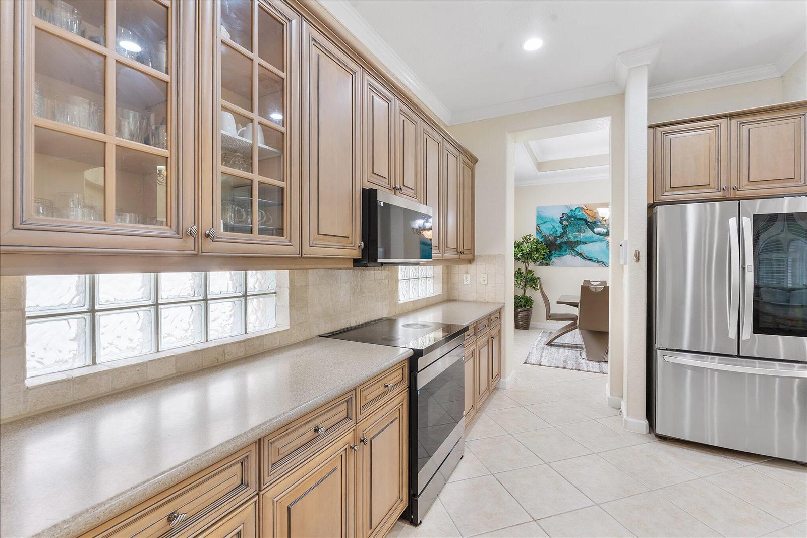 A kitchen with stainless steel appliances, wood cabinets, and tile flooring opens to a dining area — 11645 NW 71st Place, Parkland FL 33076, PARKLAND, FL