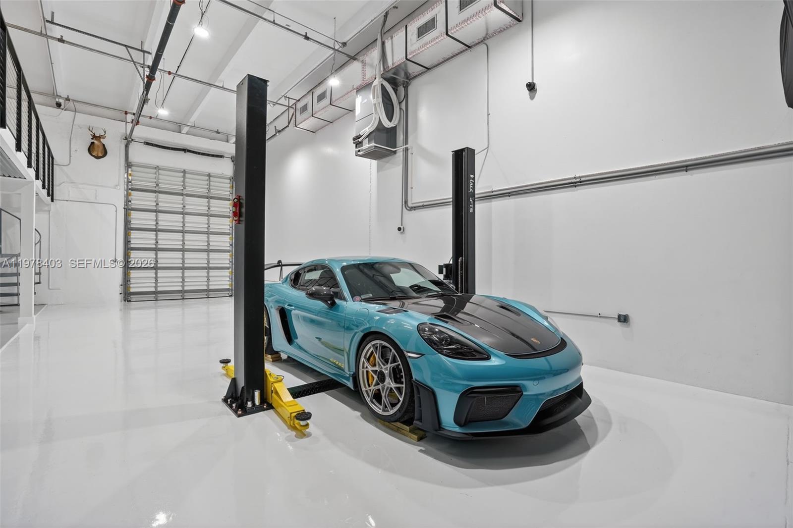 A bright garage features a teal Porsche parked on a two-post vehicle lift — 13500 SW 134th Ave # 4A, Miami FL 33186, MIAMI, FL