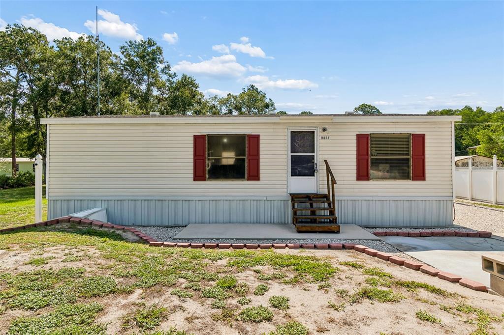 A single-story manufactured home with beige siding, red shutters, and a small wooden staircase — 10654 HOLGATE STREET, NEW PORT RICHEY, FL