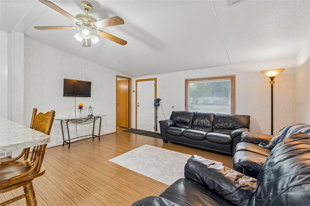 A living room features wood-look flooring, a ceiling fan, black leather sofas, and a television — 10654 HOLGATE STREET, NEW PORT RICHEY, FL