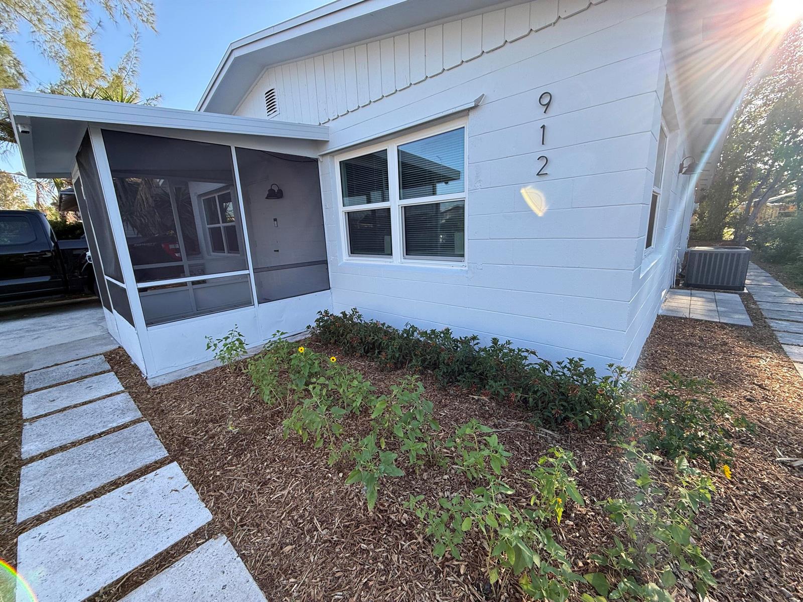 The exterior of a white house features a screened-in porch and a landscaped garden bed — 912 SE Tarpon Avenue, Stuart FL 34994, STUART, FL
