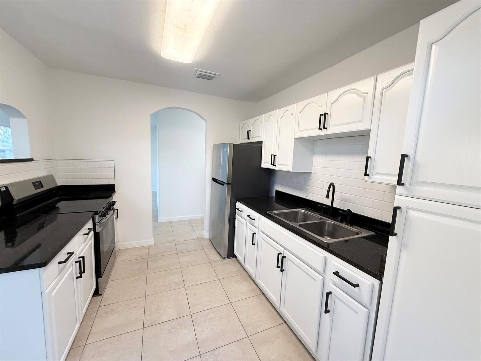 A kitchen features white cabinets, black countertops, stainless steel appliances, and light tile flooring — 912 SE Tarpon Avenue, Stuart FL 34994, STUART, FL