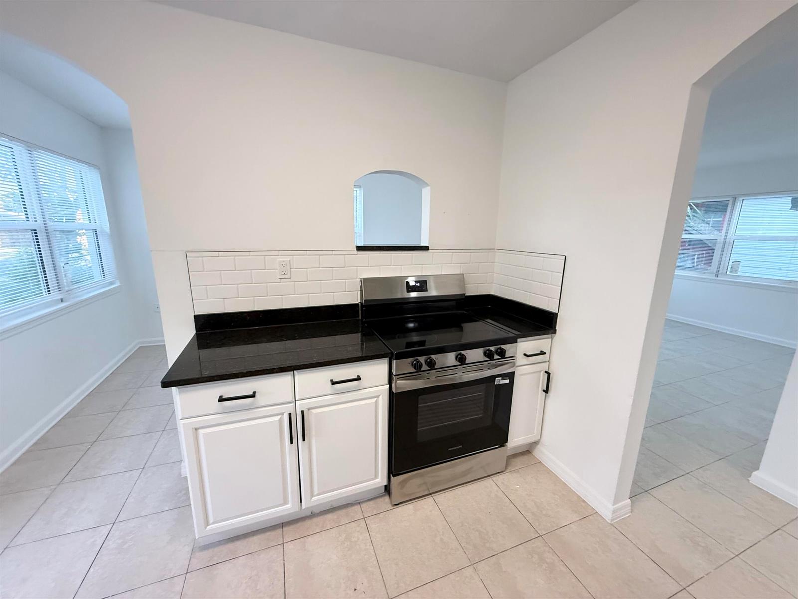 A kitchen features white cabinets, black countertops, a stainless steel stove, and white subway tile — 912 SE Tarpon Avenue, Stuart FL 34994, STUART, FL