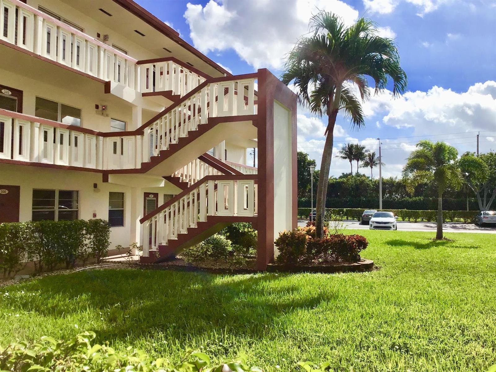 An exterior view of a multi-story apartment building featuring an outdoor staircase and palm trees — 308 Brighton H # 308, Boca Raton FL 33434, BOCA RATON, FL