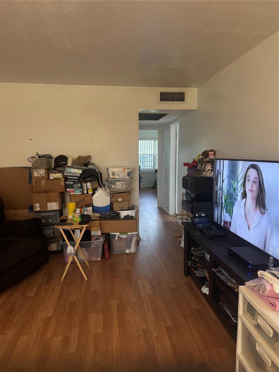 A living room with wood-look flooring, a television, and a stack of storage boxes — 308 Brighton H # 308, Boca Raton FL 33434, BOCA RATON, FL