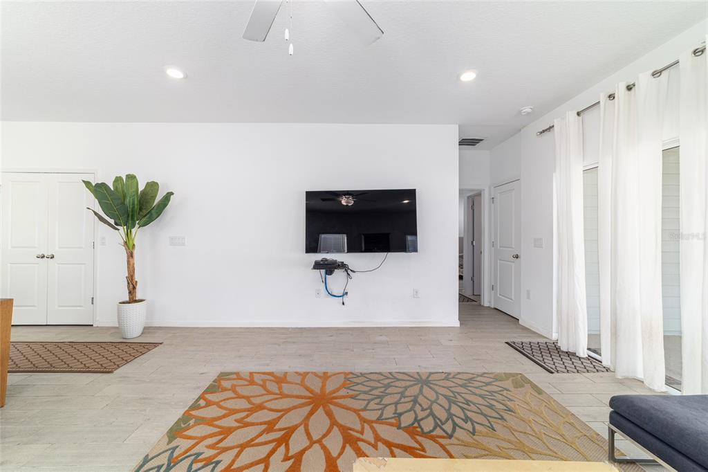 A living room features white walls, light tile flooring, a wall-mounted television, and a rug — 7451 SW 76TH TERRACE, OCALA, FL
