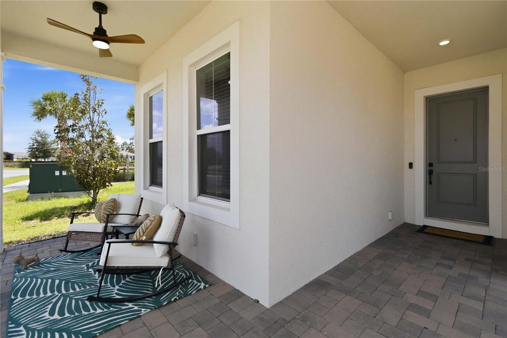 A covered front porch features a gray door, two rocking chairs, and a ceiling fan — 13092 SUNRISE HARVEST DRIVE, WINTER GARDEN, FL