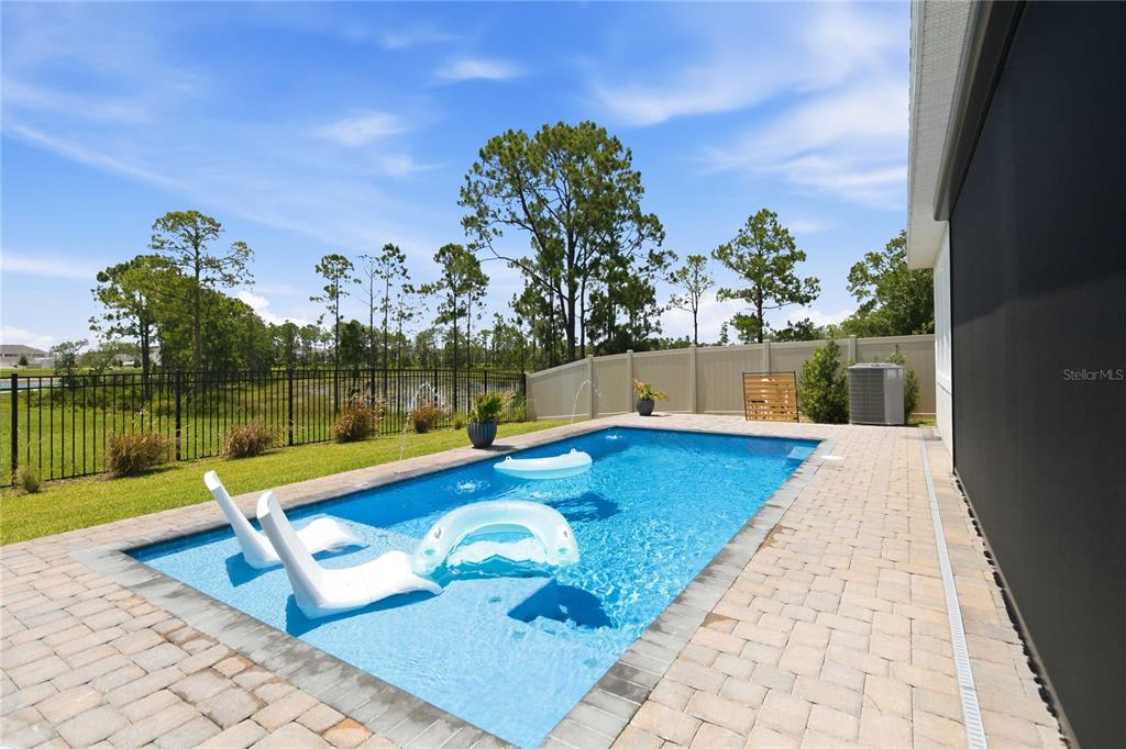 A rectangular swimming pool with lounge chairs sits on a paved patio beside a fence — 13092 SUNRISE HARVEST DRIVE, WINTER GARDEN, FL