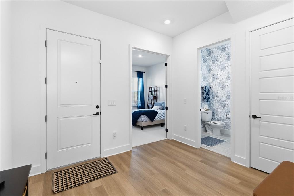 A bright entryway with wood-look flooring, a white front door, and two interior doorways — 13092 SUNRISE HARVEST DRIVE, WINTER GARDEN, FL