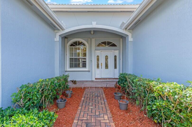 A brick walkway leads to a white front door flanked by hedges and potted plants — 2570 SE 4th Place, Homestead FL 33033, HOMESTEAD, FL