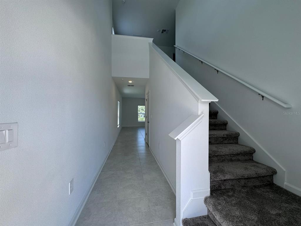 A hallway with tile flooring leads to a window, with carpeted stairs on the right — 1033 WATERFALL BOULEVARD, DAVENPORT, FL