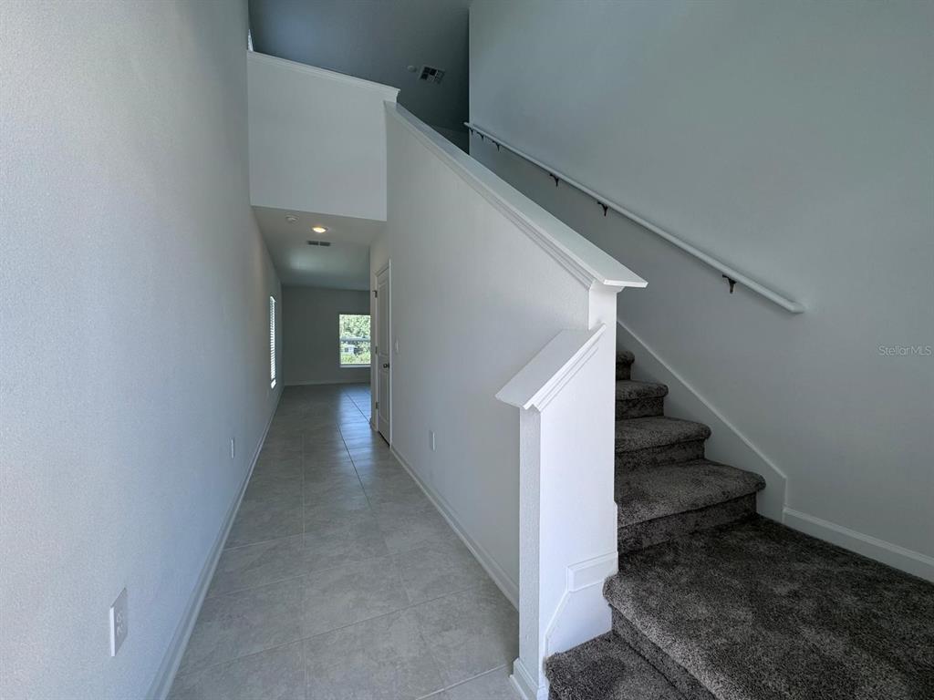 A hallway with tile flooring leads to a windowed room beside a carpeted staircase — 1033 WATERFALL BOULEVARD, DAVENPORT, FL