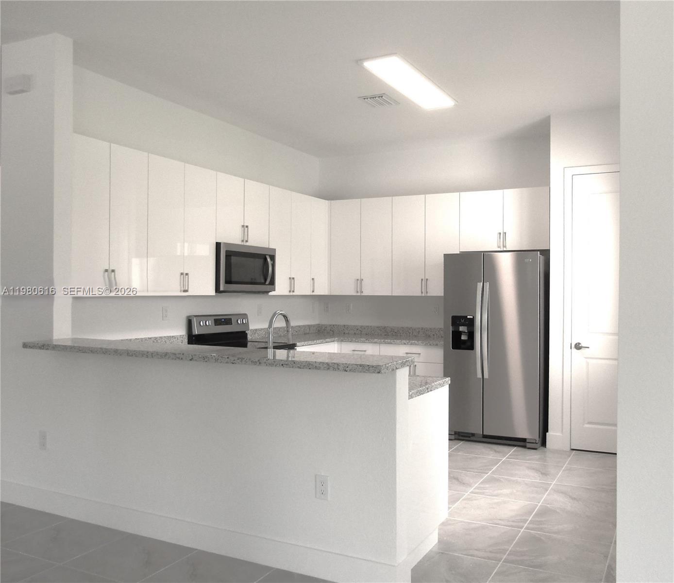 A kitchen features white cabinets, granite countertops, stainless steel appliances, and light tile flooring — 11998 SW 232nd St, Miami FL 33170, MIAMI, FL