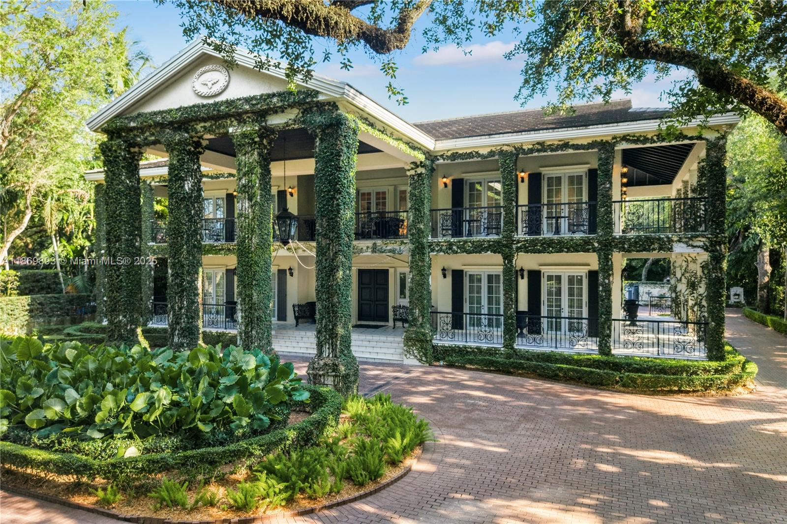 A two-story colonial-style mansion features ivy-covered columns, a brick driveway, and multiple balconies — 612 Sunset Dr, Coral Gables FL 33143, CORAL GABLES, FL