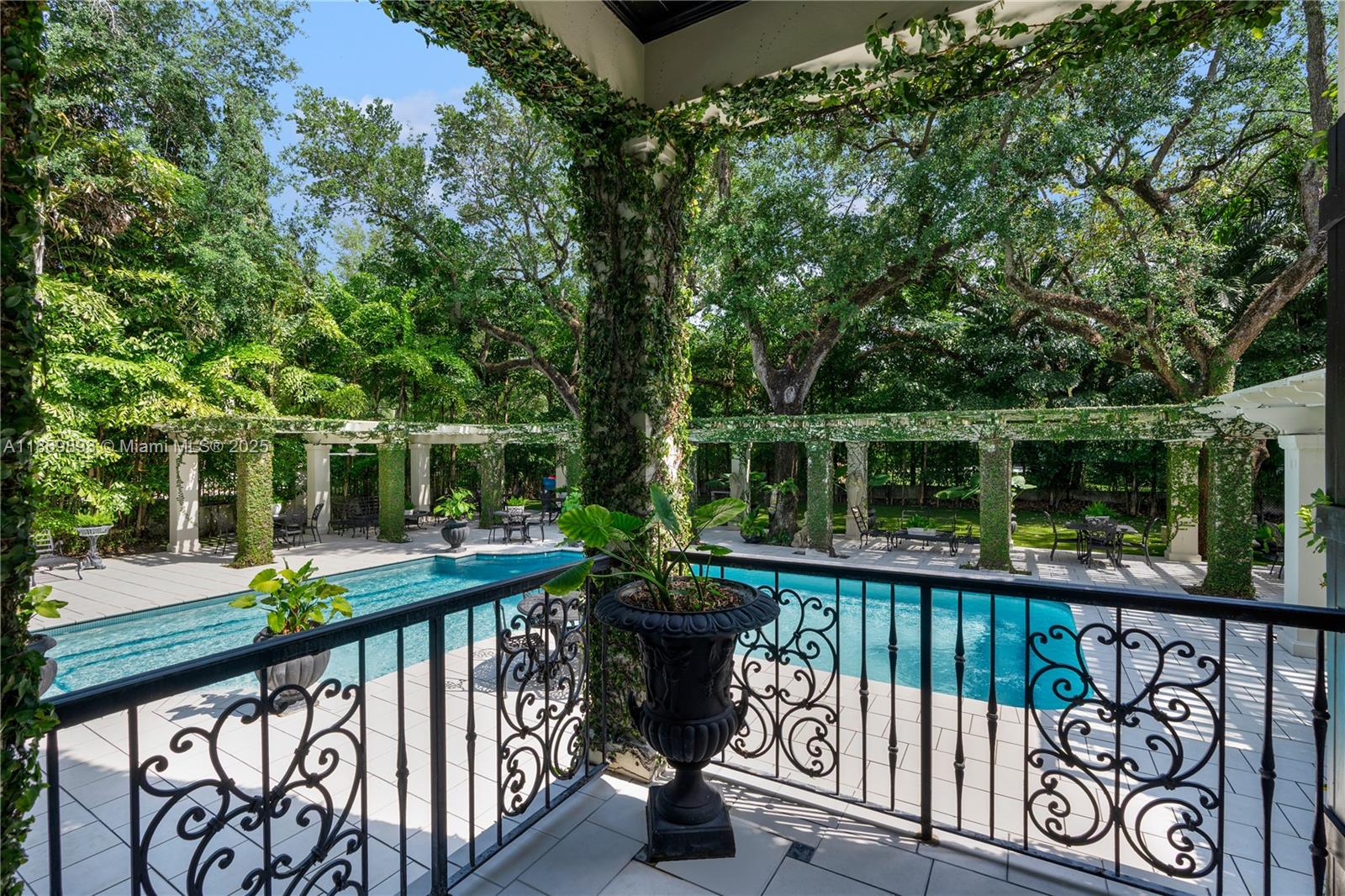 A balcony with black iron railings overlooks a swimming pool surrounded by a vine-covered pergola — 612 Sunset Dr, Coral Gables FL 33143, CORAL GABLES, FL