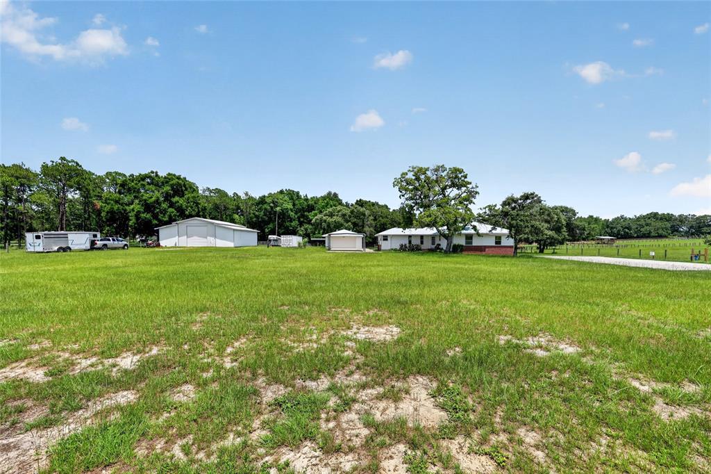 A wide, grassy field leads to a house, a large metal barn, and a smaller shed — 20500 NW 27TH STREET, MORRISTON, FL