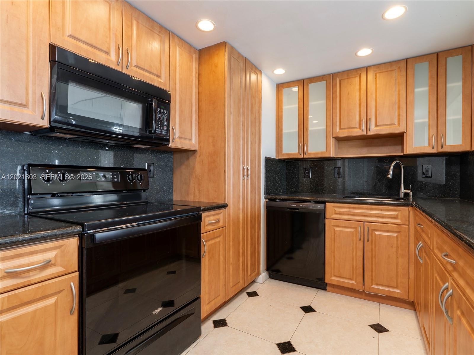 A kitchen features light wood cabinets, black appliances, dark granite countertops, and tiled flooring — 11111 Biscayne Blvd # 912, Miami FL 33181, MIAMI, FL