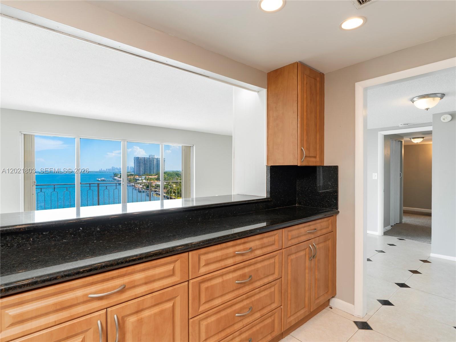 A kitchen features wood cabinets, black granite countertops, and a pass-through window overlooking the ocean — 11111 Biscayne Blvd # 912, Miami FL 33181, MIAMI, FL