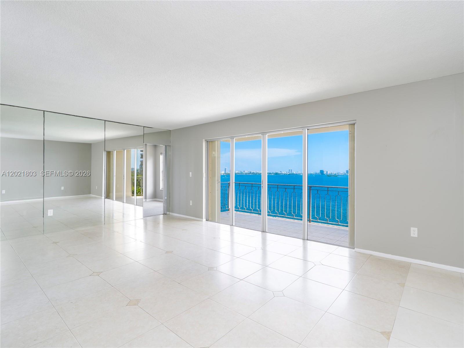 An empty room with tiled floors, mirrored walls, and a balcony overlooking the ocean — 11111 Biscayne Blvd # 912, Miami FL 33181, MIAMI, FL
