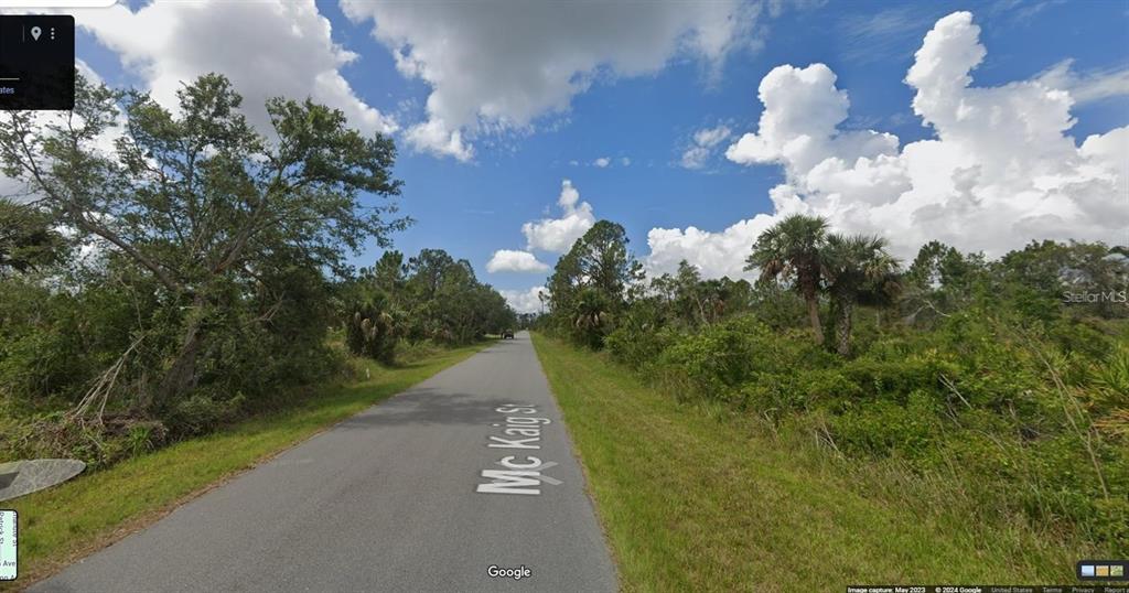A paved road stretches through a wooded area with dense vegetation under a cloudy sky — 2278 MCKAIG STREET, PORT CHARLOTTE, FL