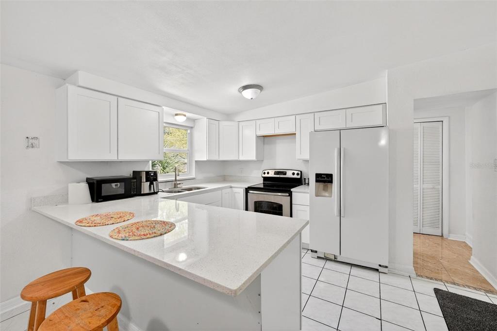 A white kitchen features a quartz peninsula, white cabinetry, stainless steel appliances, and tile flooring — 410 SANTIAGO AVENUE, ORLANDO, FL