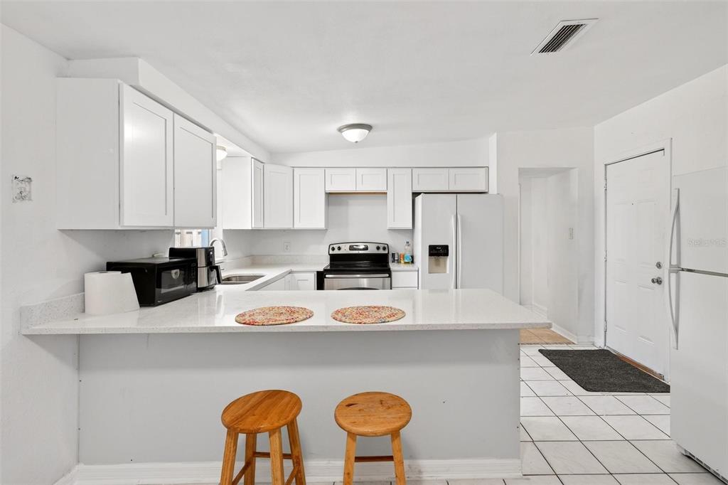 A kitchen with white cabinets, stainless steel appliances, a breakfast bar, and white tile flooring — 410 SANTIAGO AVENUE, ORLANDO, FL
