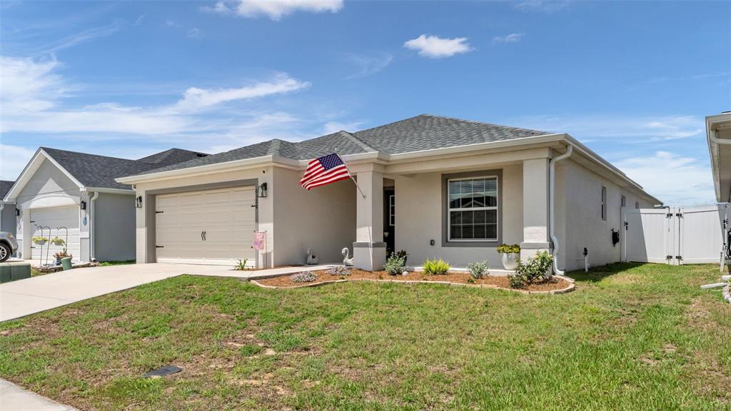 A single-story suburban house with a beige stucco exterior, a two-car garage, and an American flag — 6328 GARDNER DRIVE, LAKELAND, FL