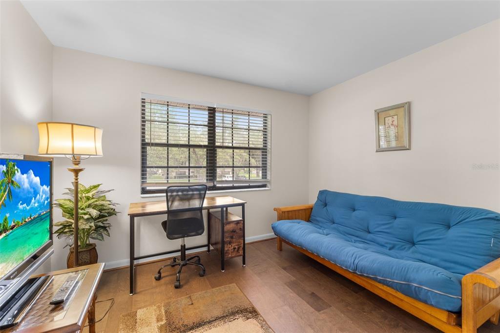 A room with wood flooring, a blue futon, a desk with a chair, and a television — 19505 QUESADA AVENUE UNIT C201, PORT CHARLOTTE, FL