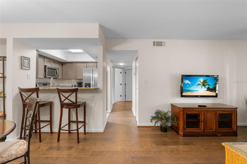 A living room with wood flooring, a wall-mounted television, and a kitchen breakfast bar — 19505 QUESADA AVENUE UNIT C201, PORT CHARLOTTE, FL