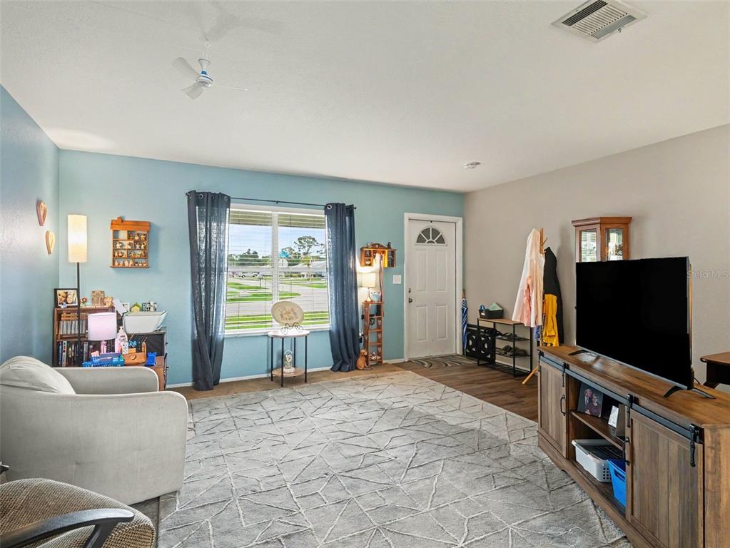 A living room features a light blue accent wall, a large area rug, and a television — 2473 FAIRBROOK STREET, NORTH PORT, FL