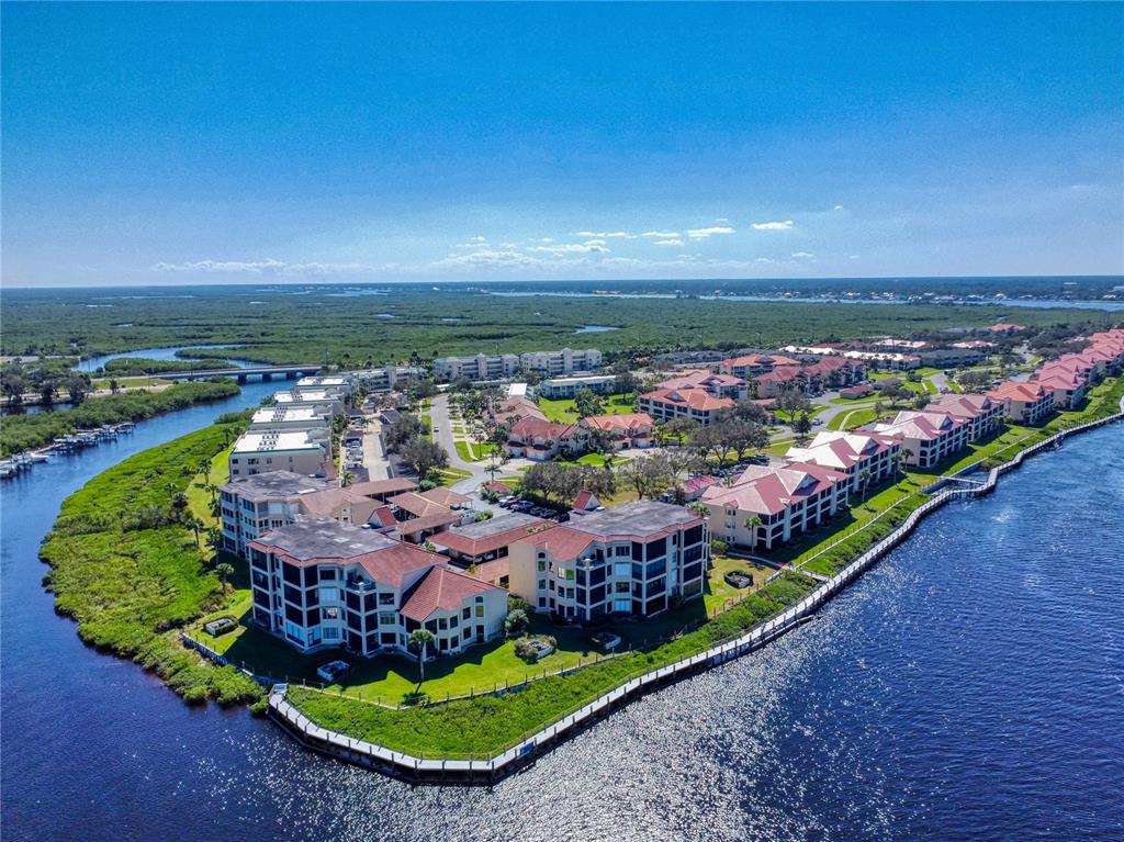 An aerial view shows a waterfront condominium complex surrounded by marshland and a river — 451 BOUCHELLE DRIVE UNIT 104, NEW SMYRNA BEACH, FL