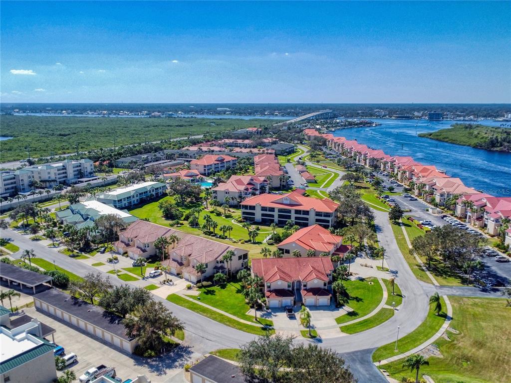 An aerial view shows a residential complex with red-roofed buildings near a coastal waterway — 451 BOUCHELLE DRIVE UNIT 104, NEW SMYRNA BEACH, FL