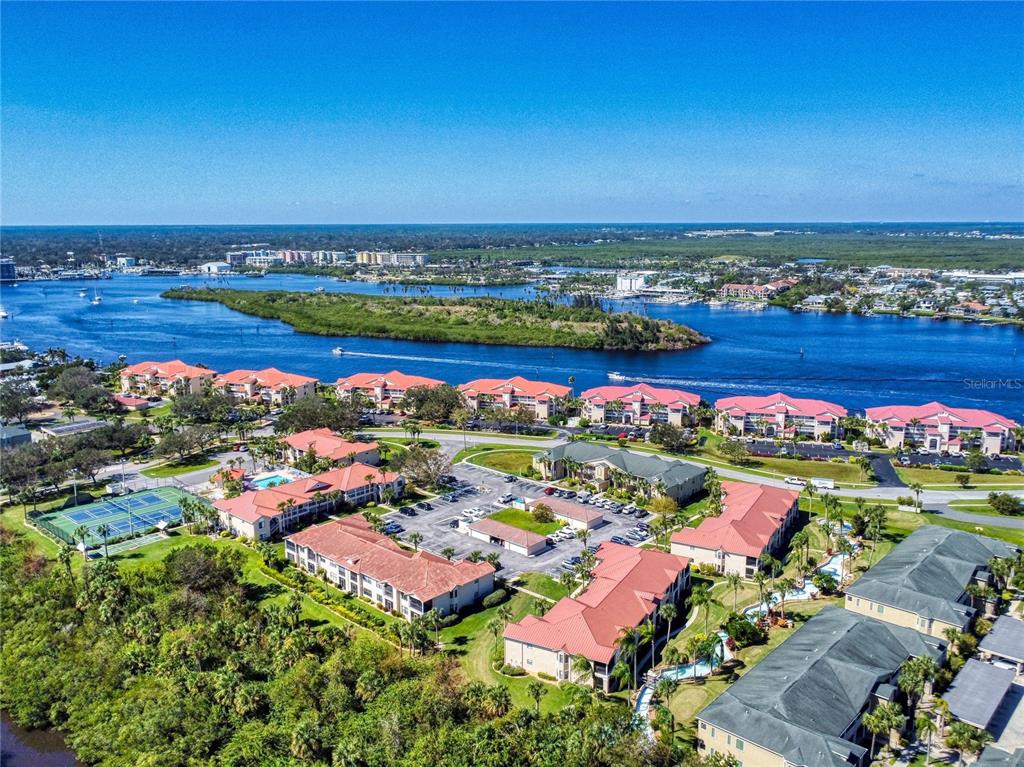 An aerial view shows a multi-building residential complex with red roofs near a waterway — 451 BOUCHELLE DRIVE UNIT 104, NEW SMYRNA BEACH, FL