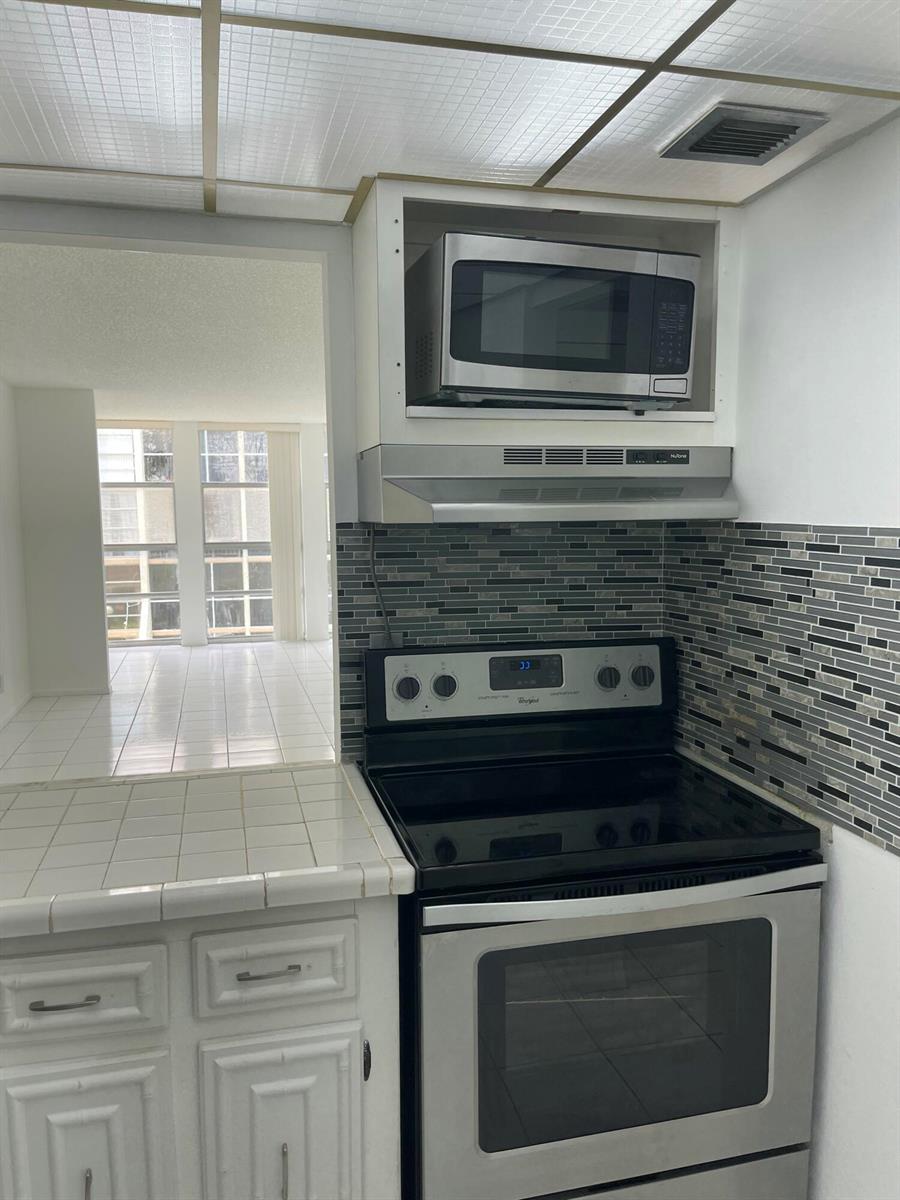 A kitchen features a stainless steel stove, a microwave, and a gray tiled backsplash — 801 Three Island Boulevard # 306, FL 33009, FL