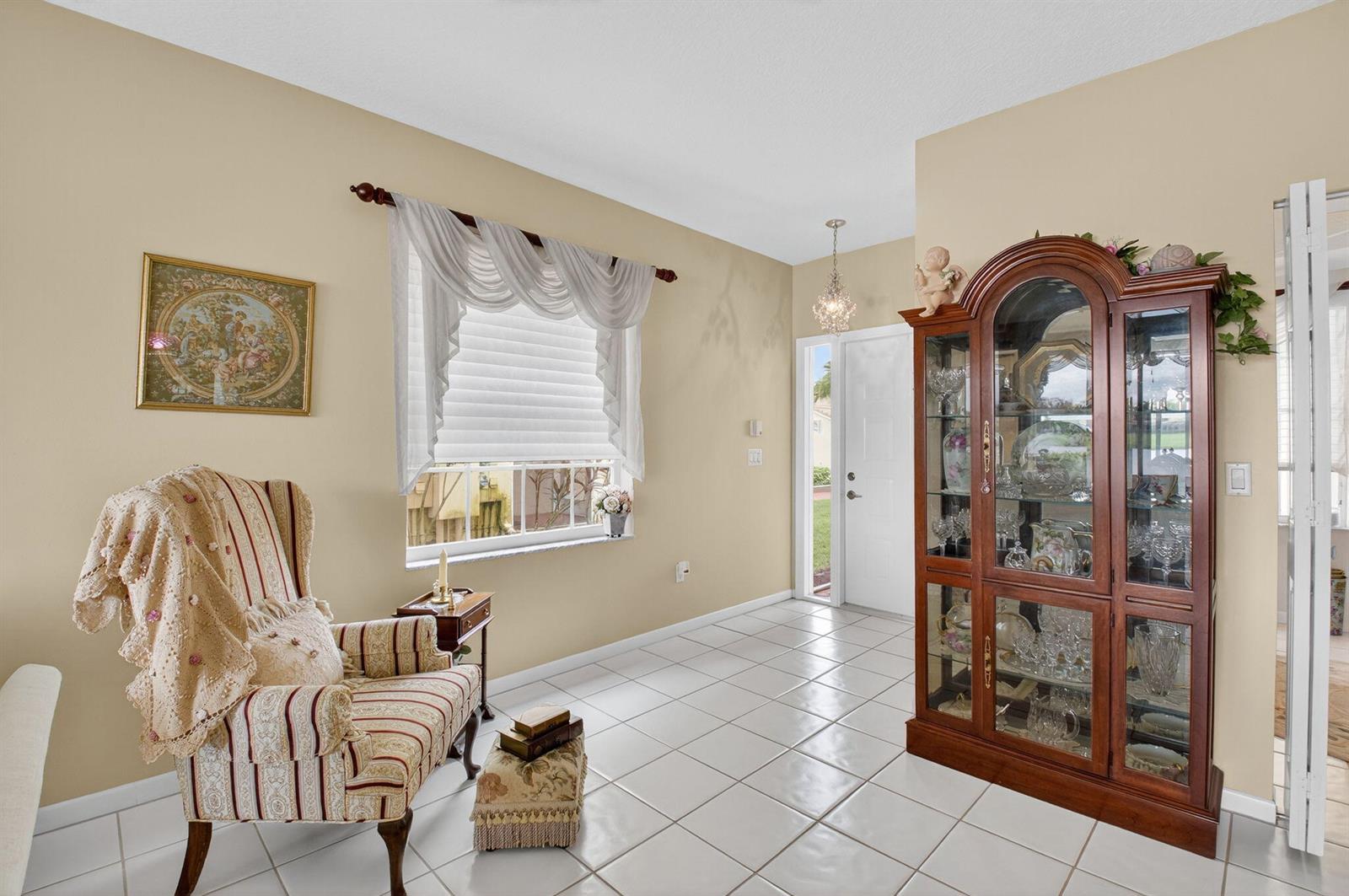 A bright entryway features white tile floors, a striped armchair, and a large wooden display cabinet — 17287 Boca Club Boulevard # 1, Boca Raton FL 33487, BOCA RATON, FL