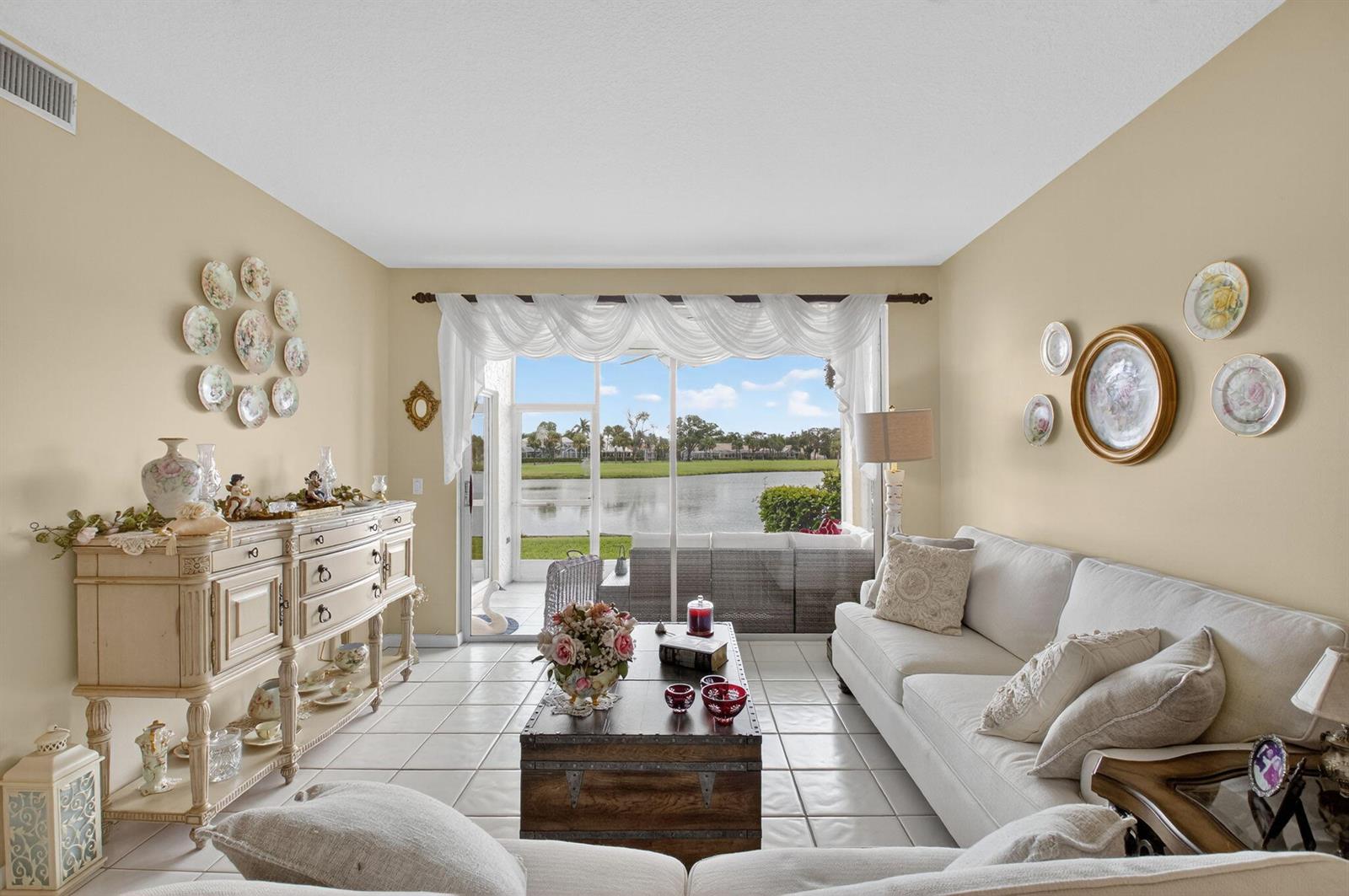 A living room features beige walls, tile flooring, a white sofa, and a lake view — 17287 Boca Club Boulevard # 1, Boca Raton FL 33487, BOCA RATON, FL