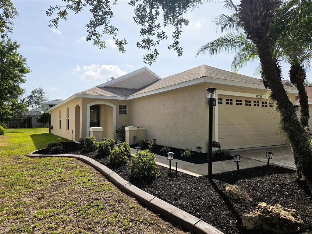 A single-story house with a beige stucco exterior, a two-car garage, and landscaped front beds — 14224 GNATCATCHER TERRACE, BRADENTON, FL