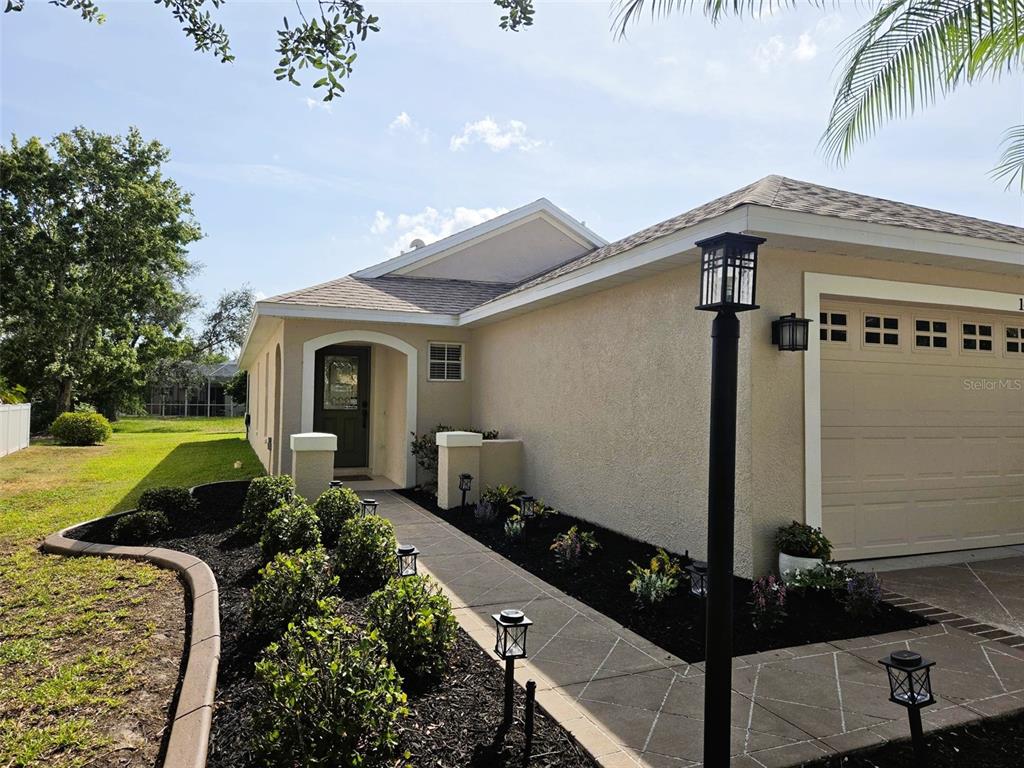 A beige house exterior features a garage, a front walkway, and landscaped garden beds — 14224 GNATCATCHER TERRACE, BRADENTON, FL