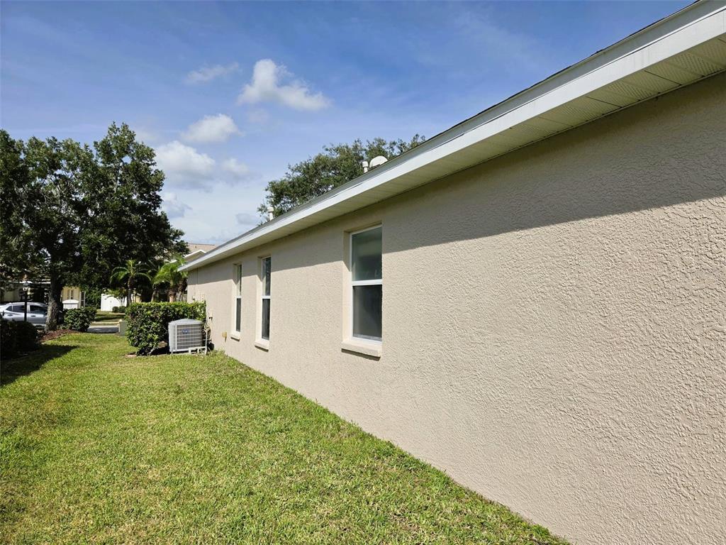 The exterior side of a beige stucco house features three windows and an air conditioning unit — 14224 GNATCATCHER TERRACE, BRADENTON, FL