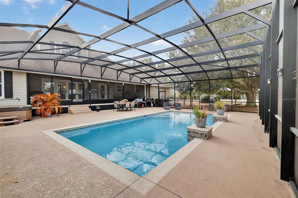 A screened-in patio features a rectangular swimming pool, a hot tub, and outdoor dining furniture — 4564 COUNTY ROAD 103G, OXFORD, FL