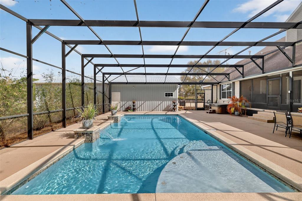 A screened-in swimming pool with water features sits on a patio next to a house — 4564 COUNTY ROAD 103G, OXFORD, FL