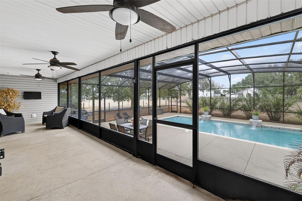 A covered patio with ceiling fans overlooks a screened-in swimming pool and backyard — 4564 COUNTY ROAD 103G, OXFORD, FL