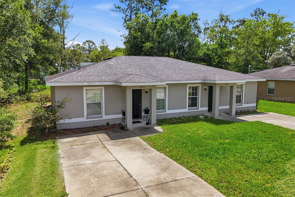 A single-story duplex with a gray exterior, concrete driveway, and a grassy front yard — 9271 N PEACHTREE WAY, CITRUS SPRINGS, FL