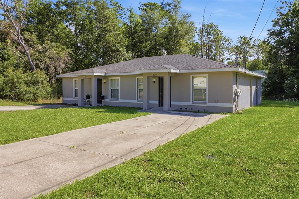 A single-story duplex with a concrete driveway and a grassy yard under a blue sky — 9271 N PEACHTREE WAY, CITRUS SPRINGS, FL